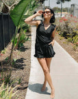 Model showcasing a stylish black one-piece swimsuit, perfect for women's summer swimwear, in a sunny outdoor setting.