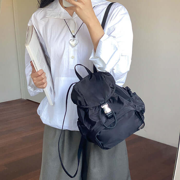 Stylish black nylon small backpack worn casually, perfect for school or everyday use, paired with a white shirt and gray bottom.