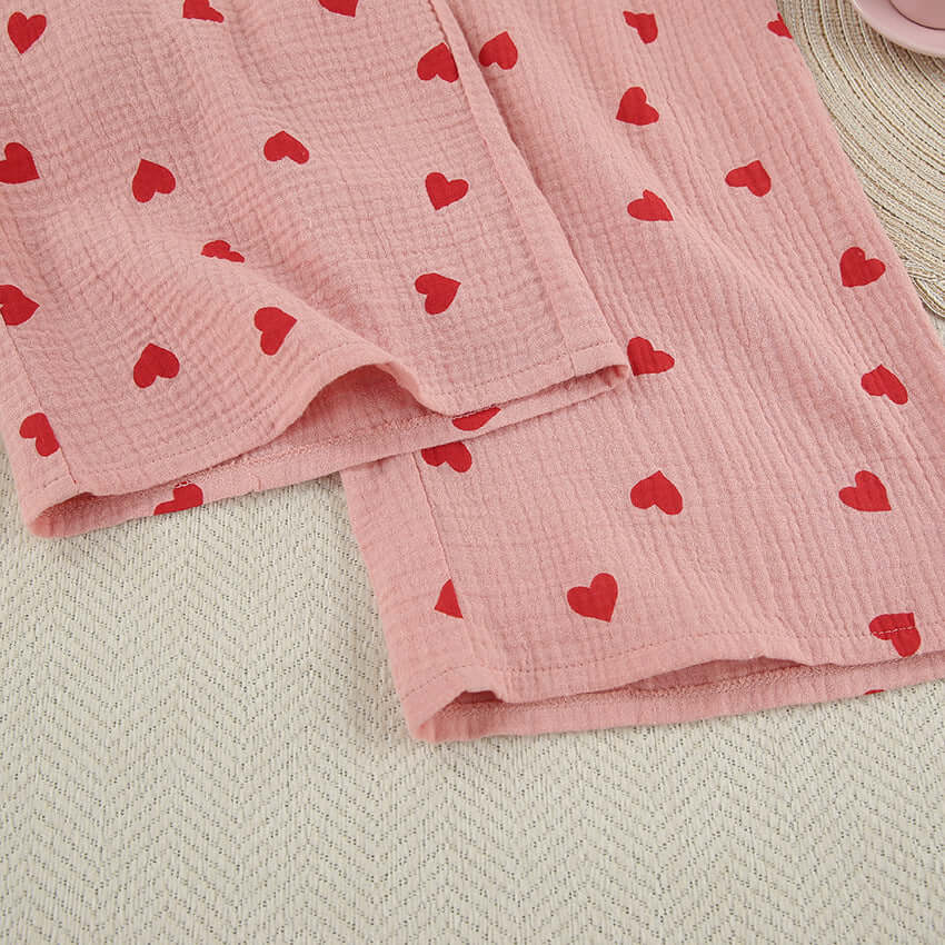 Cotton pajama fabric in soft pink with red heart patterns for a cozy nightwear look.