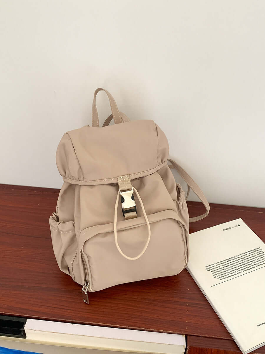 Simple small nylon backpack in beige, perfect for casual use or school, featuring adjustable straps and multiple pockets.