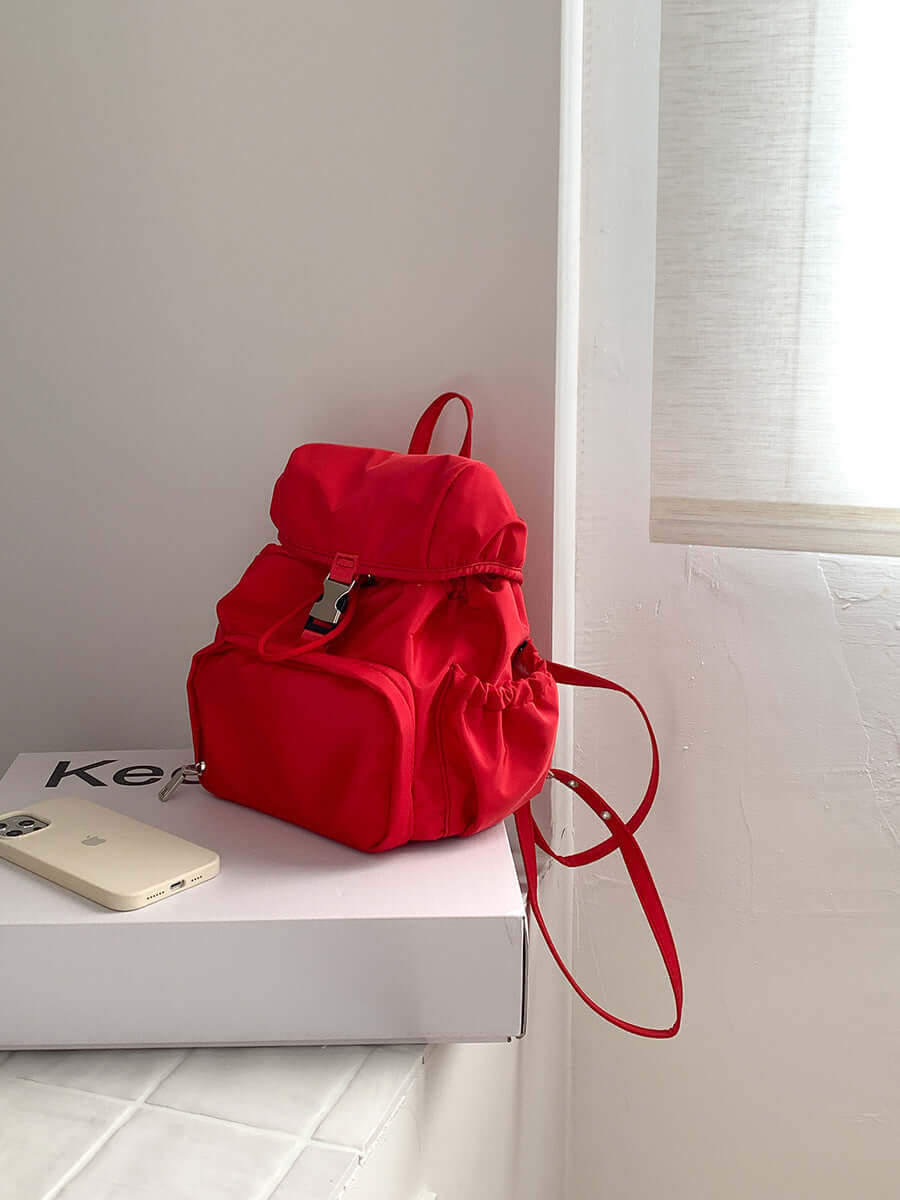 Red nylon small backpack on a white table, showcasing its casual and fashionable design for school or daily use.