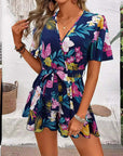 Woman wearing a floral printed navy jumpsuit with ruffle sleeves, perfect for summer beach vacations.