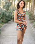 Woman in a floral print one-piece swimsuit smiling outdoors, ideal for summer beach outings.