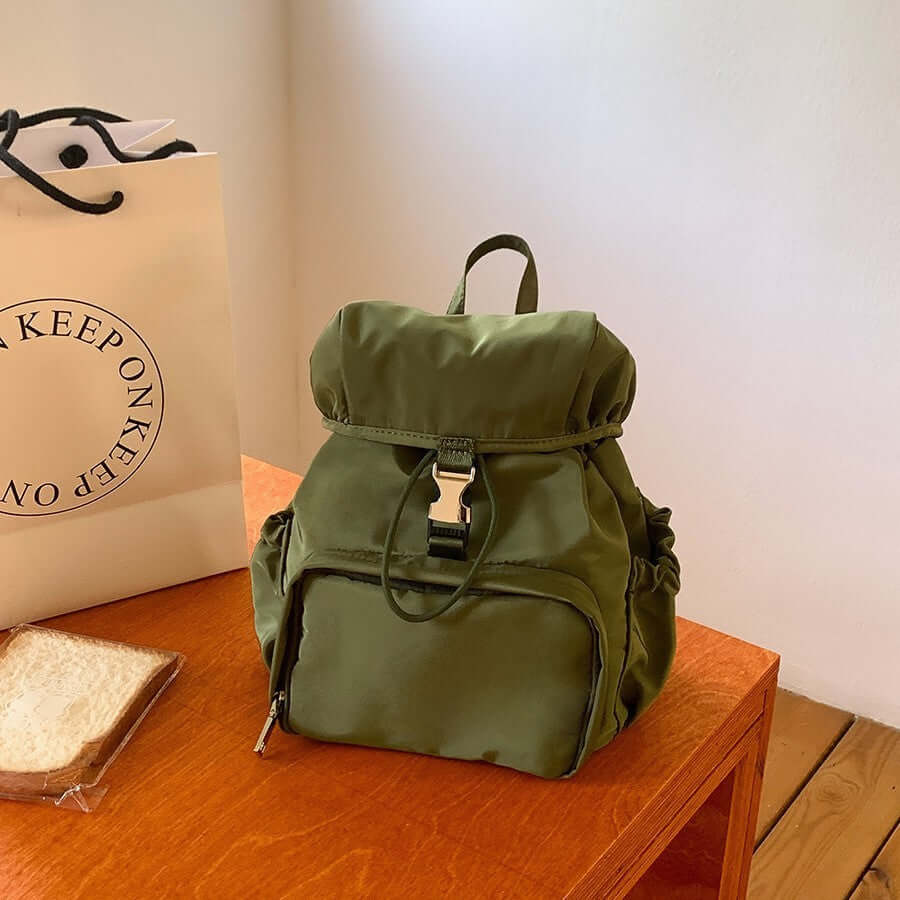 Green nylon casual backpack on a wooden table with bread, perfect for school and fashion use.