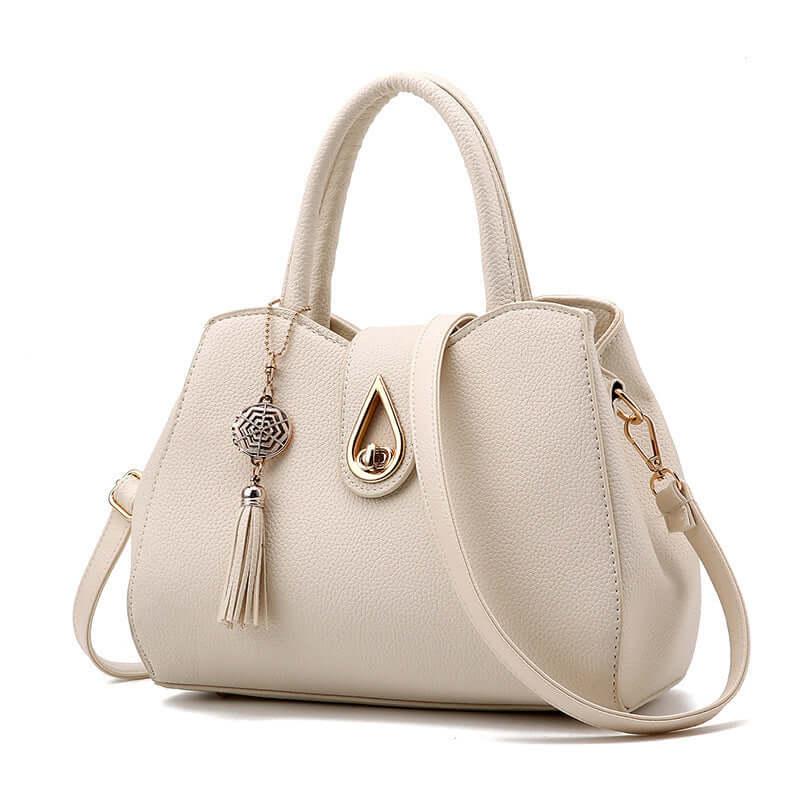 Stylish women's handbag in cream PU leather with tassel and decorative charm, featuring a zipper opening and shell shape.