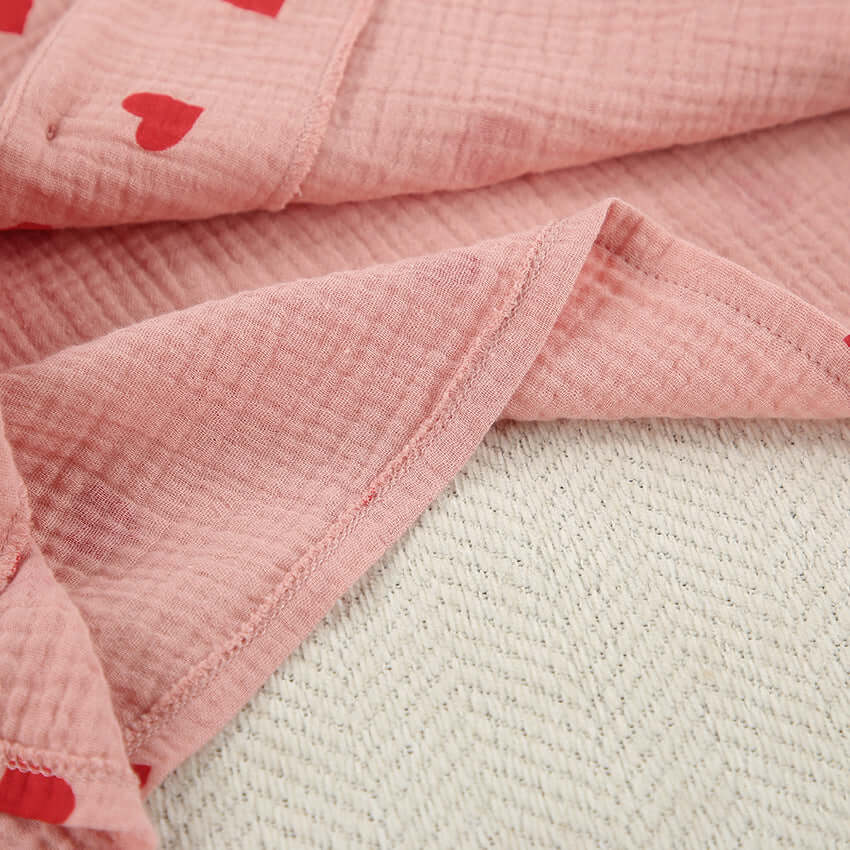 Close-up of soft pink cotton fabric with red heart prints, showcasing delicate craftsmanship and texture.