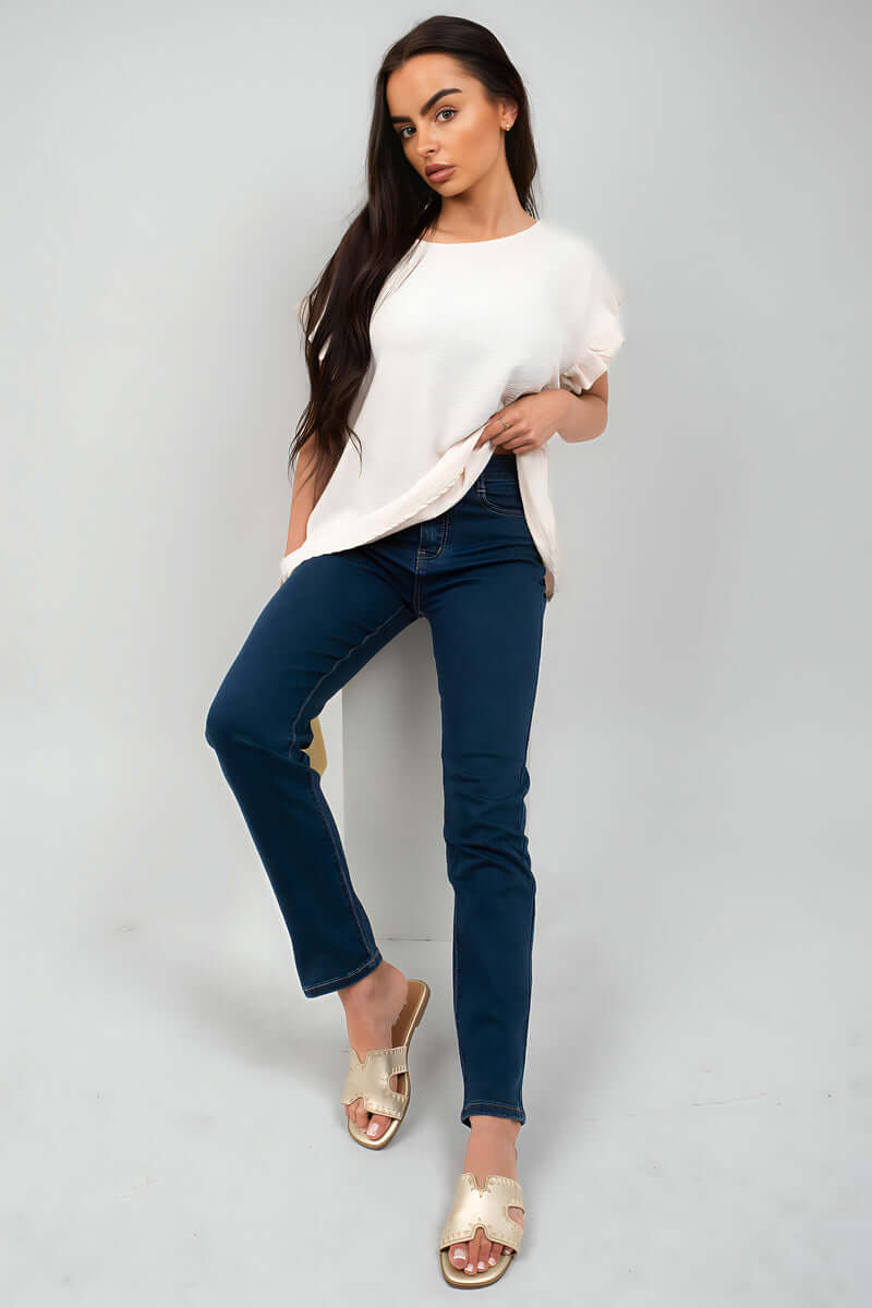 Woman in straight leg high waist jeans paired with a white top and sandals, showcasing casual style.