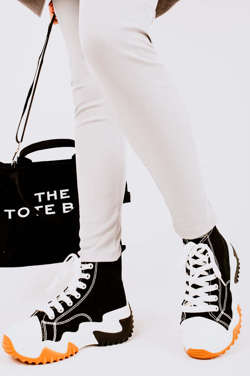 Stylish chunky platform trainers with black and white design, paired with light leggings and a black tote bag.