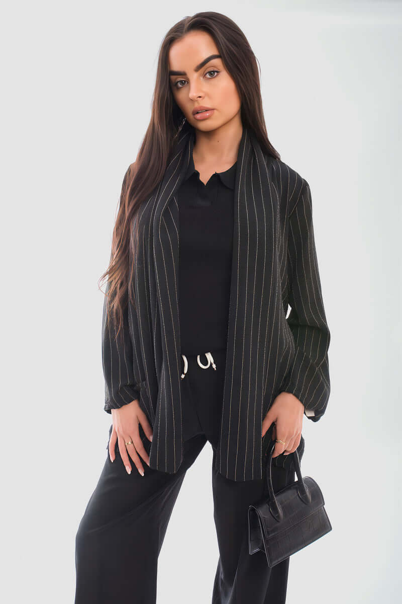 Model wearing a black striped long sleeve cardigan over a black outfit, holding a small bag.