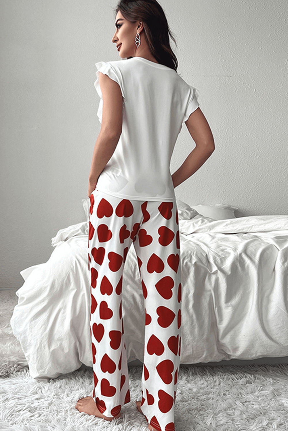 Back view of a woman wearing a red heart print pants lounge set with a ruffled white tank top.
