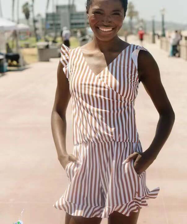 Model wearing a striped one-piece swimsuit, showcasing stylish ruffles and vibrant summer colors at the beach.