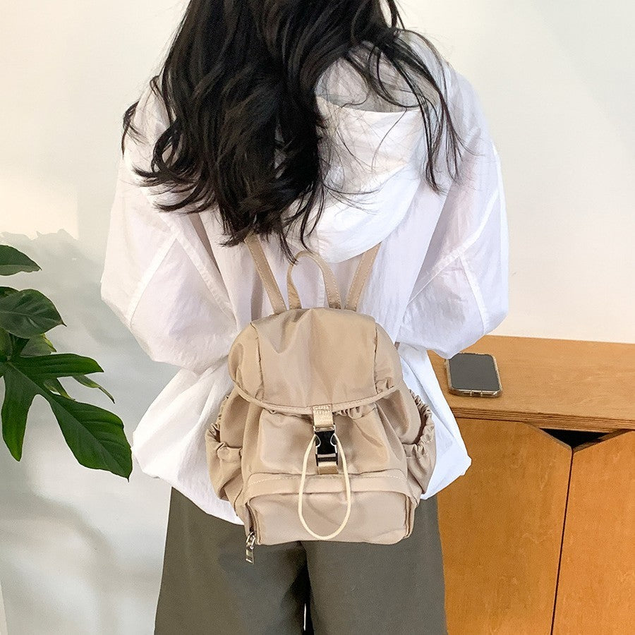 Stylish small nylon backpack in beige worn by a female, perfect for casual outings or school.