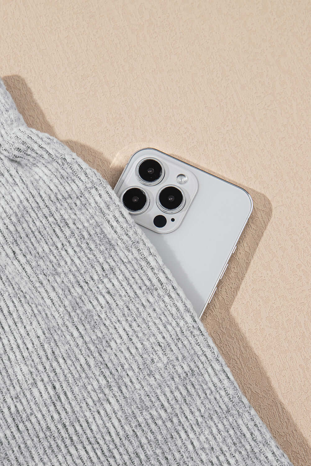 Close-up of light grey ribbed fabric with a smart phone partially visible, showcasing modern lounge wear and tech.