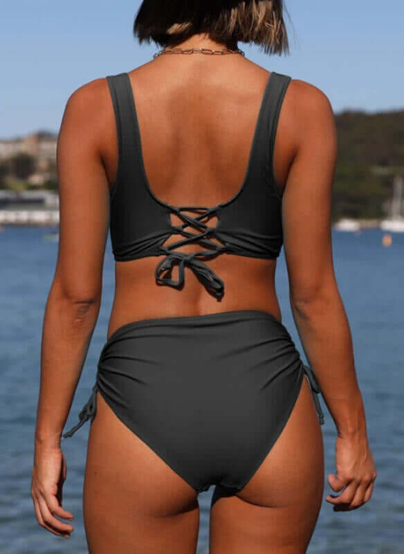 Back view of a woman in a stylish strappy bikini swimsuit by the beach, showcasing comfortable women's swimwear.