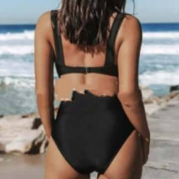 Back view of a woman wearing a women's solid color black bikini by the beach, showcasing summer swimwear.