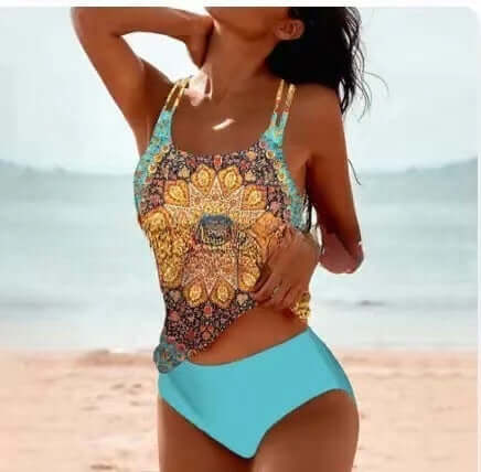Model wearing a vibrant women&#39;s swimwear swimsuit with a colorful print and blue bottom on the beach.