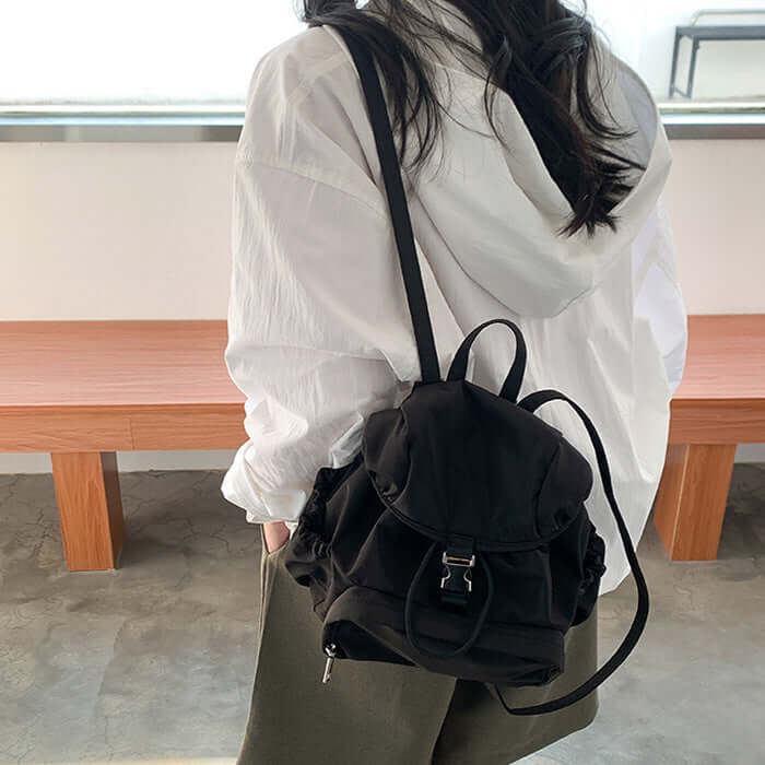 Stylish female wearing a black nylon simple small backpack casual schoolbag in a modern interior.