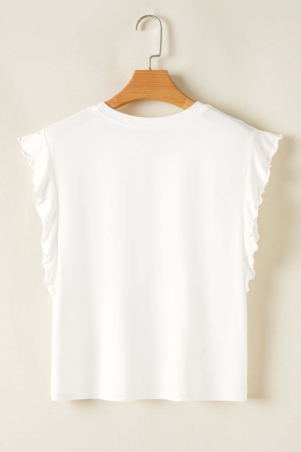 White ruffled tank top hanging on a wooden hanger against a neutral background.