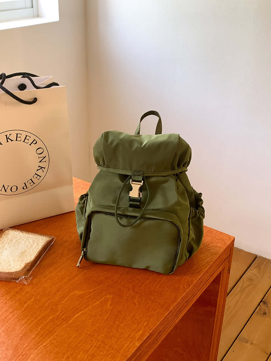 Small green nylon backpack on a wooden table, casual fashion schoolbag for women.