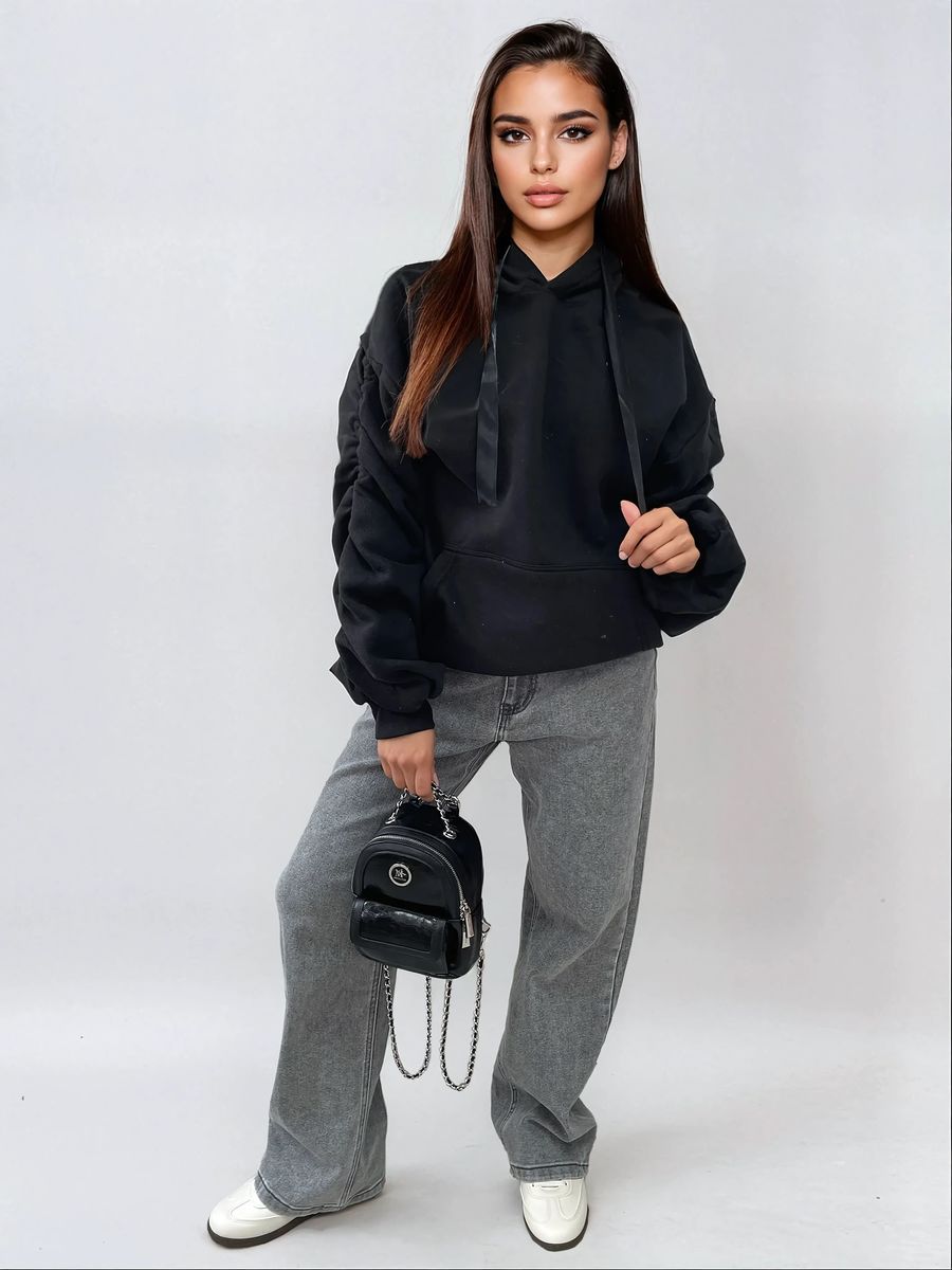 Stylish model wearing a black ruched sleeve oversized hoodie with front pouch pocket and grey wide-leg jeans.