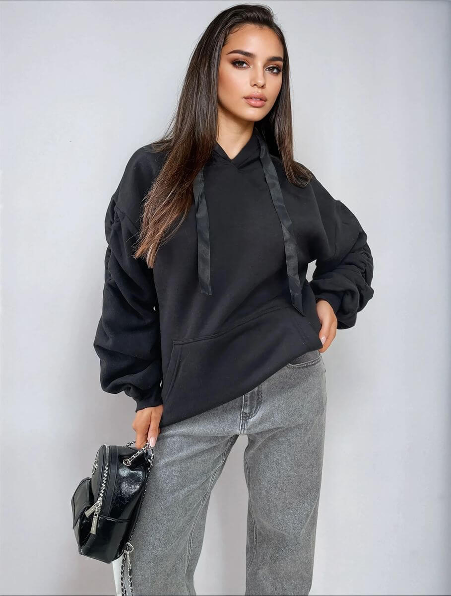 Model wearing a black ruched sleeve oversized hoodie with front pouch pocket and stylish gray jeans.