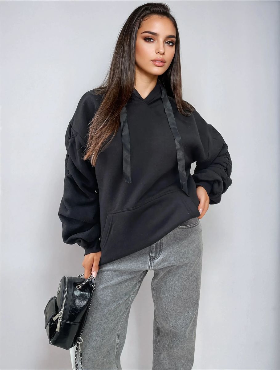 Model wearing a black ruched sleeve oversized hoodie with front pouch pocket and stylish gray jeans.