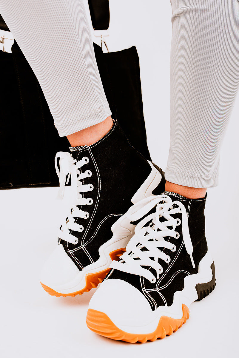 Black and white chunky platform lace-up trainers worn with casual pants, perfect for a stylish everyday look.