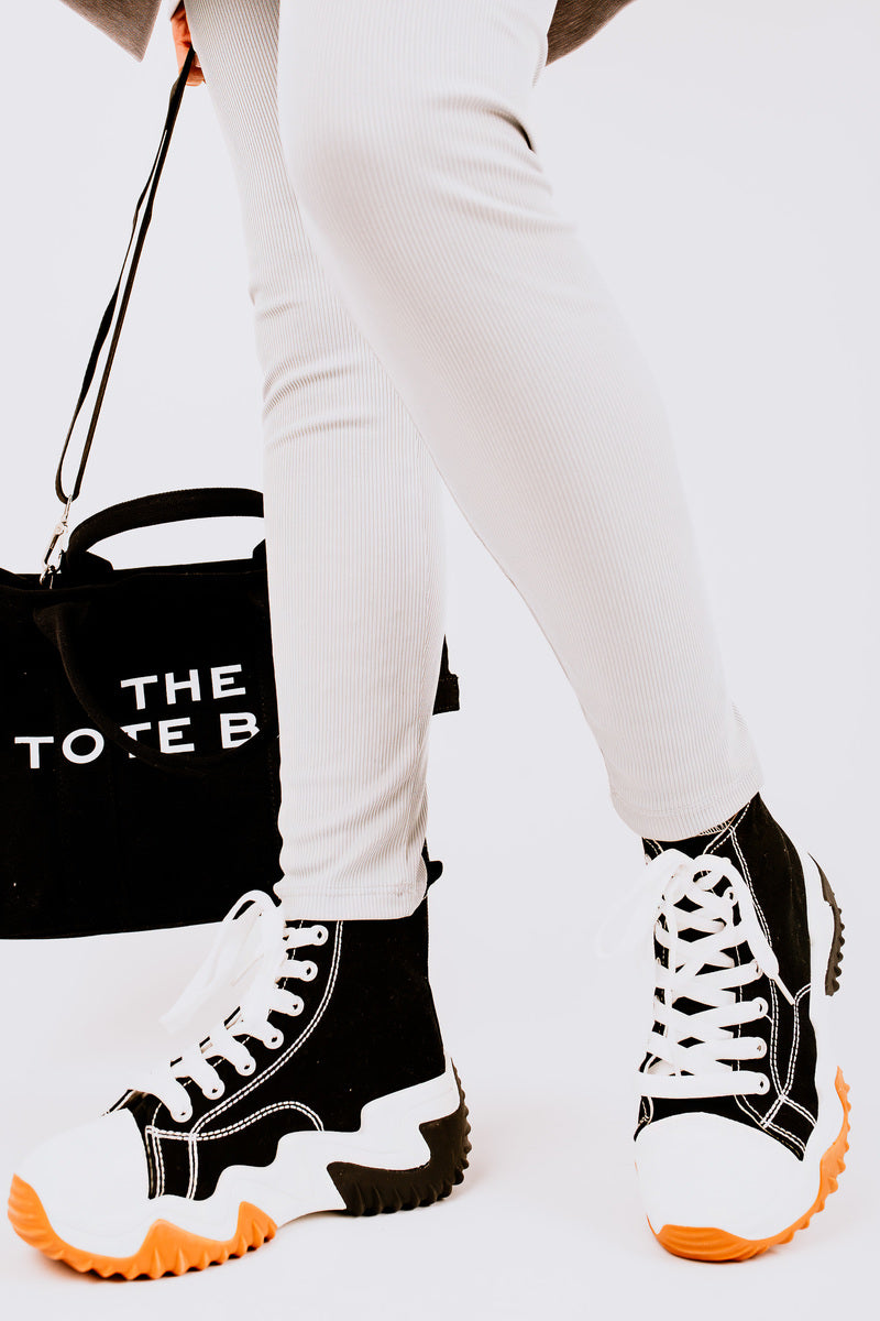 Stylish chunky platform trainers with black and white design, paired with light leggings and a black tote bag.