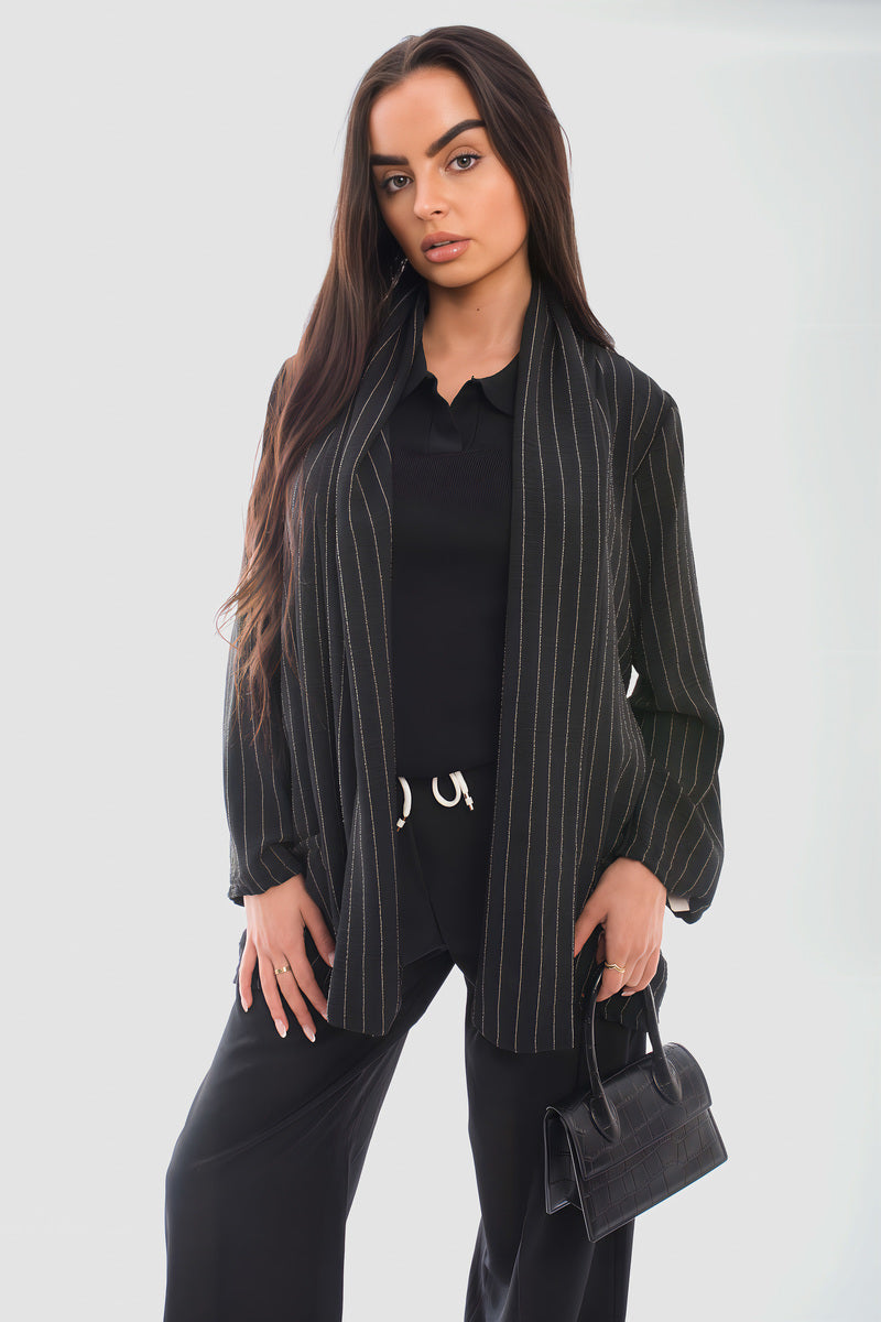 Model wearing a black striped long sleeve cardigan over a black outfit, holding a small bag.