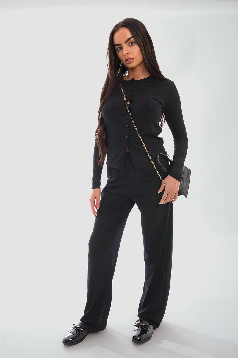 Model wearing a stylish black long sleeve button down top and trouser co-ord set, featuring a chic crossbody bag and sneakers.
